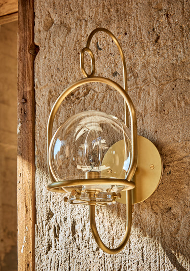 Robert True Ogden RTO Lighting - Small Emil Lantern Sconce - Brushed Satin Brass - 6" Clear Glass Globe - Hung Outside on a Concrete Wall#finish_brushed-satin-brass #glass_clear-glass